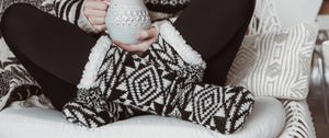Woman having a warm cup of tea snuggled up on a chair wearing tall warm Scandinavian style slipper socks by Muk Luks