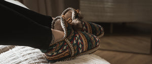 Girl wearing muk luks amira slipper with all over fairisle pattern sitting on bed in a sun bathed room